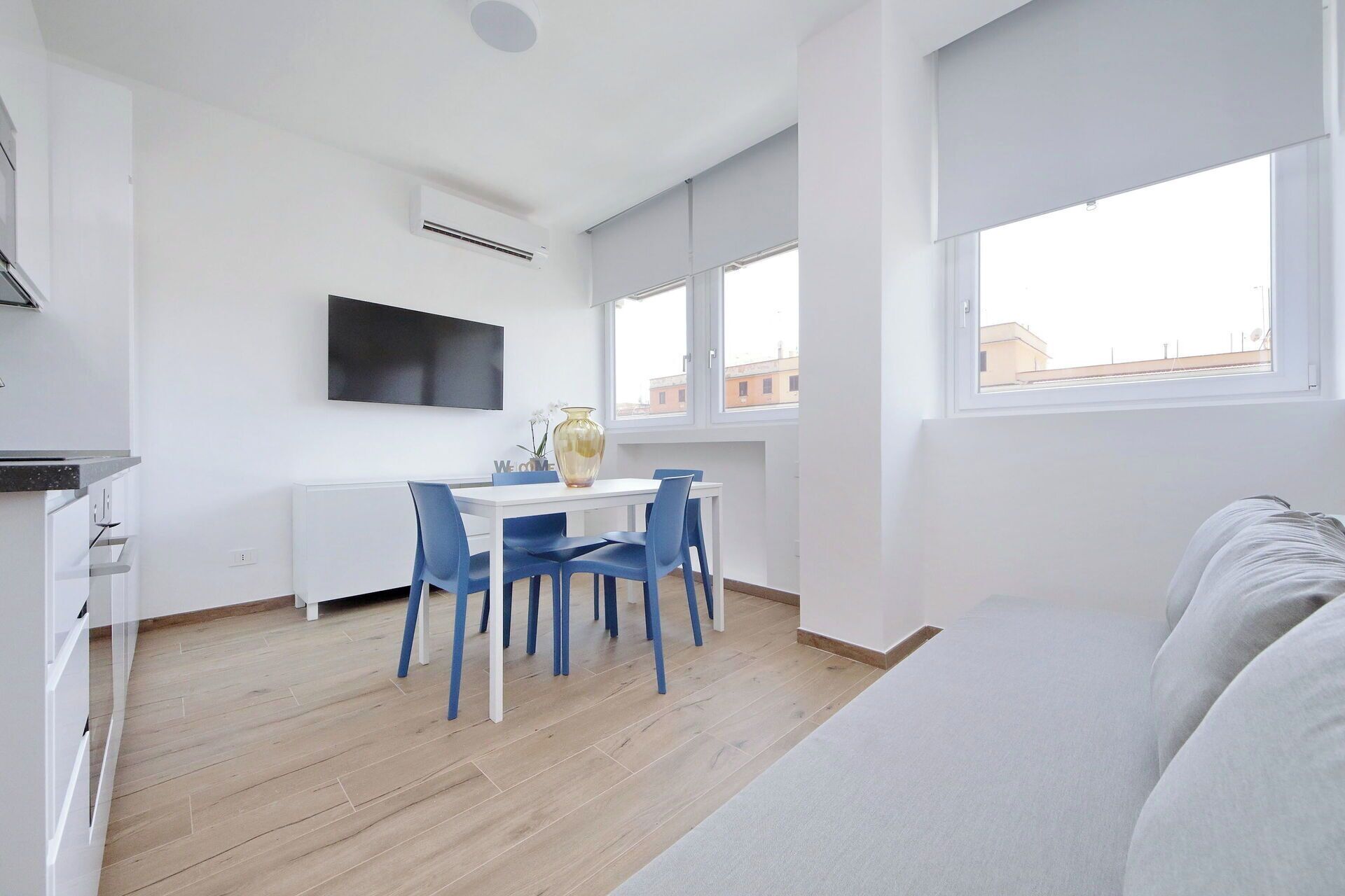 Ein modernes Wohnzimmer mit Essbereich, einem wandmontierten Flachbildfernseher und einem großen Fenster mit Blick auf die Stadt.