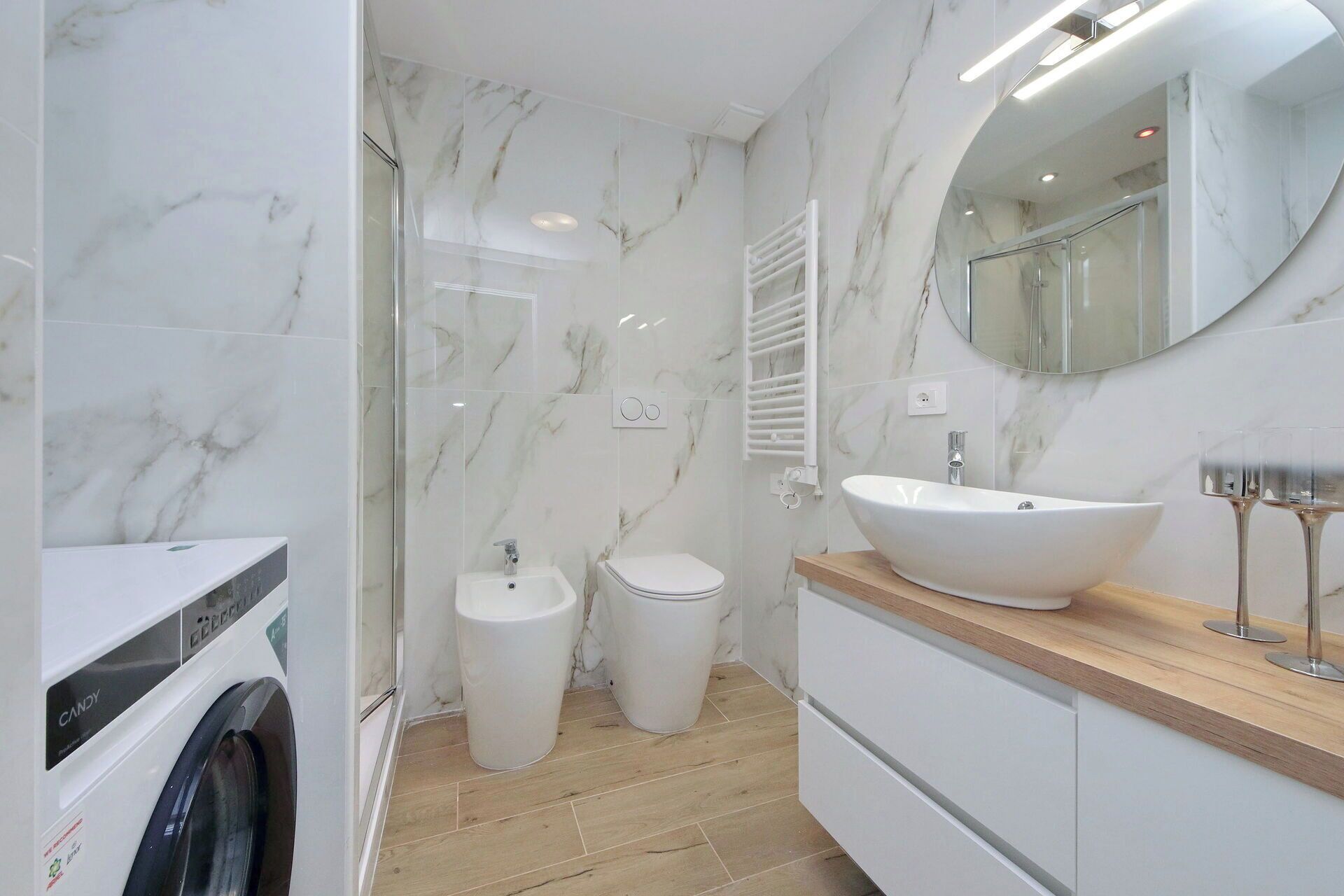 A modern bathroom with a marble wall, a large sink, a mirror, and a built-in washing machine.