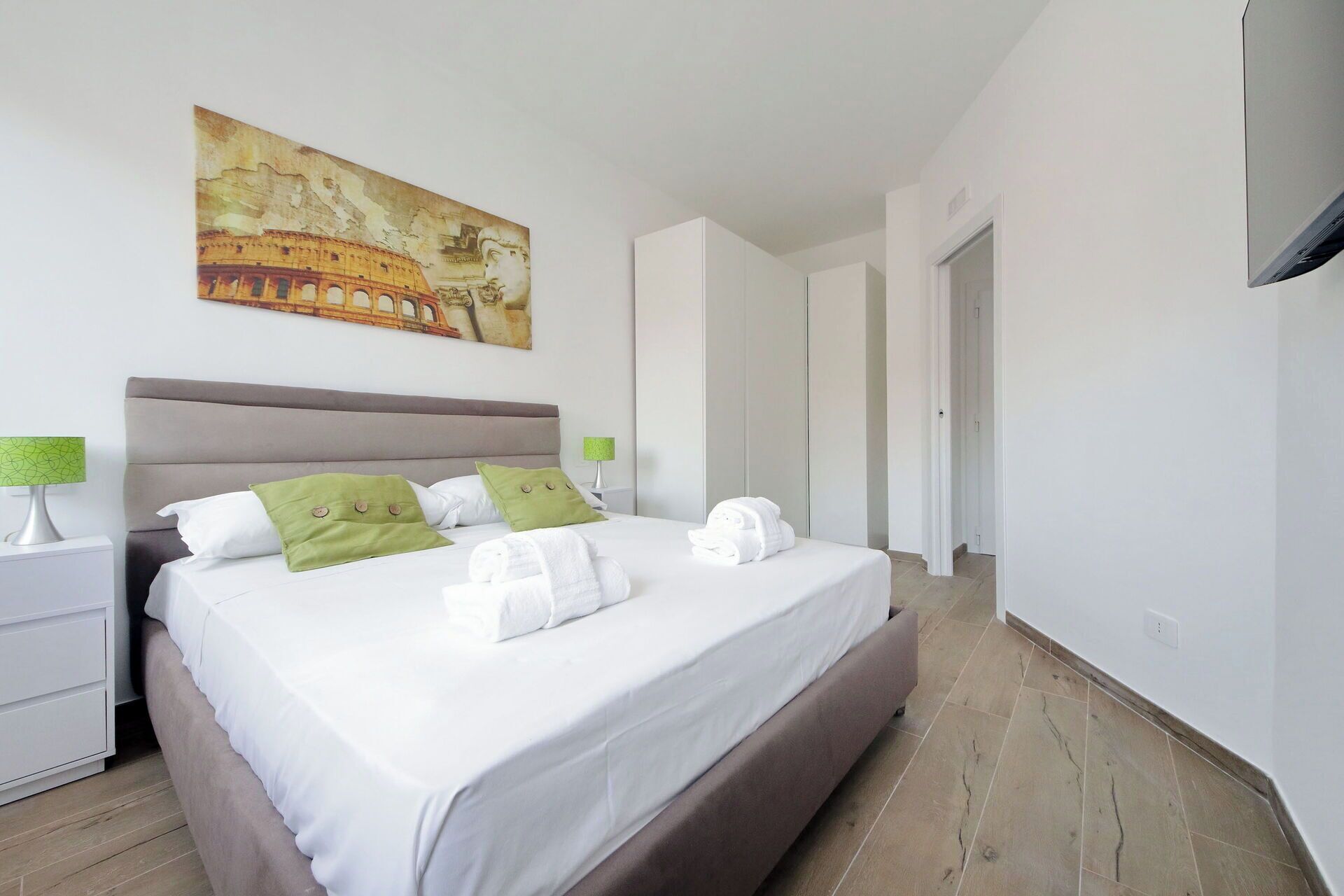 Hotelkamer met een groot bed, nachtkastje, schilderij en een deur naar een andere kamer.