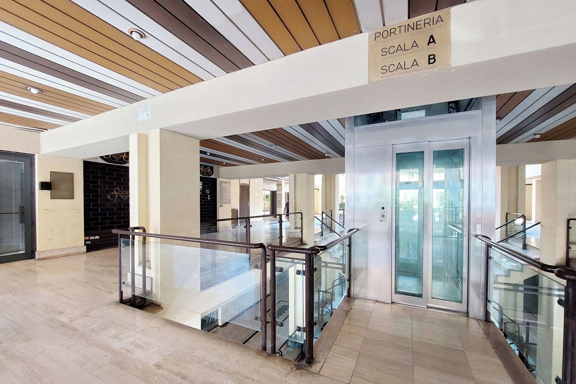 Een modern interieur met een glazen balustrade, een bordje met 'PORTINERIA' en een trap.