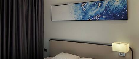 Una habitación de hotel moderna con una cama, una mesita de noche, una lámpara de pared y una lámpara del techo, junto con un cuadro abstracto grande.