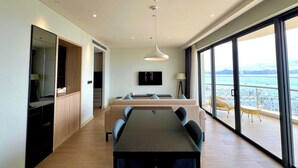 Une chambre d’hôtel moderne dotée d’un coin repas, d’une grande fenêtre offrant une vue sur la ville et d’un balcon aménagé avec du mobilier d’extérieur.