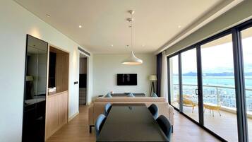 A modern hotel room with a dining area, a large window with a city view, and a balcony with outdoor furniture.