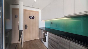 A modern kitchen with a built-in washing machine, wooden cabinets, and a green backsplash. - CMH Homestay A side - 5star standard (Halong City)