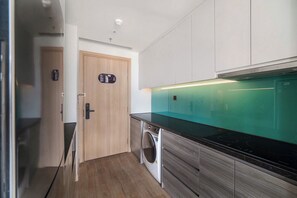 A modern kitchen with a built-in washing machine, wooden cabinets, and a green backsplash. - CMH Homestay A side - 5star standard (Halong City)
