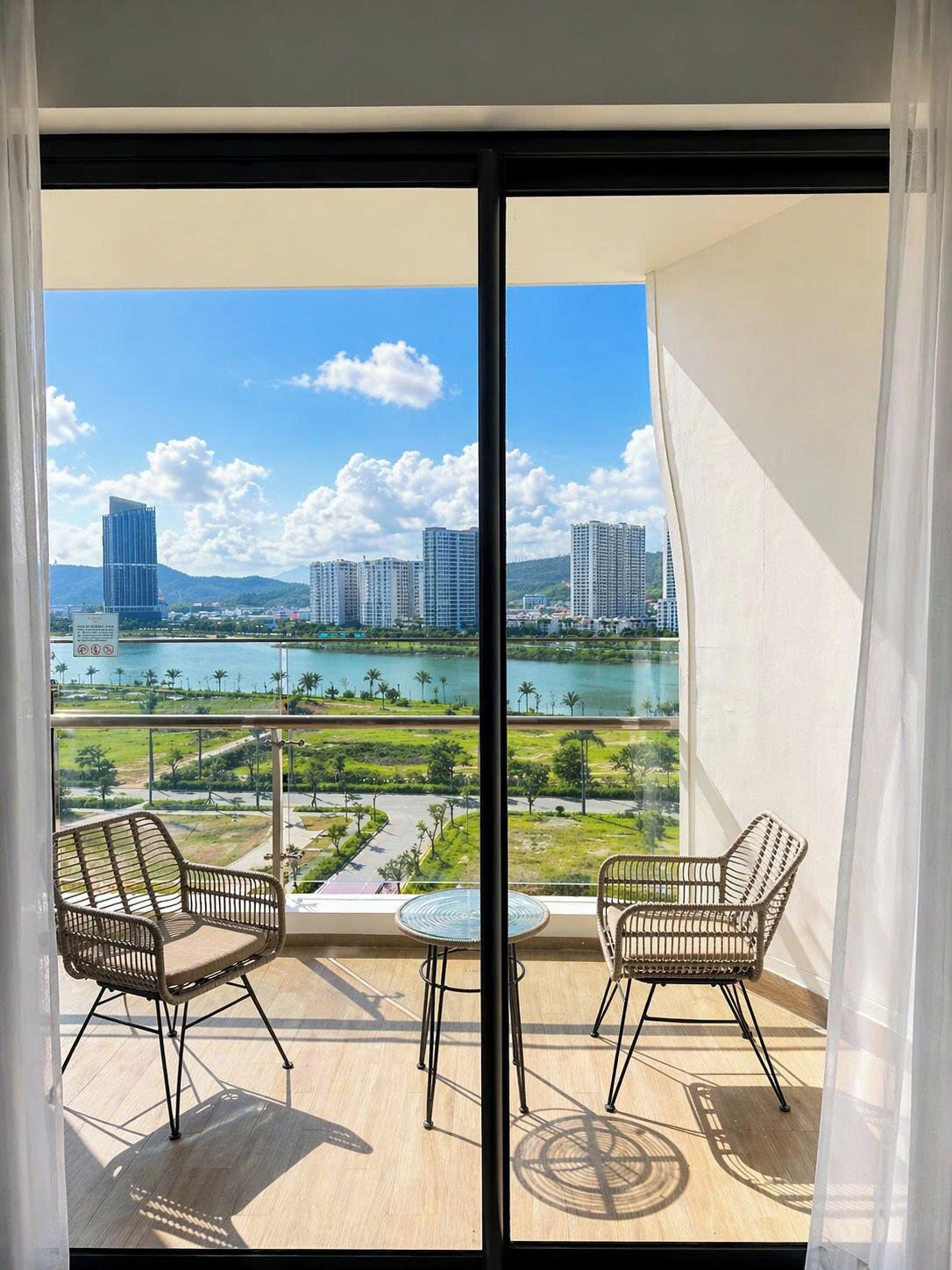 Ein Balkon mit zwei Korbstühlen und einem kleinen Tisch, mit Blick auf ein Gewässer und Gebäude.