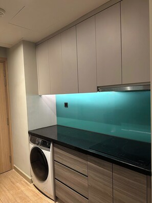 A modern kitchen with a built-in washing machine, grey cabinets, and a black countertop. - CMH Homestay A side - 5star standard (Halong City)