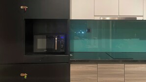 Une cuisine moderne dotée d’un four à micro-ondes encastré, d’une hotte en acier inoxydable et de meubles de rangement en bois.