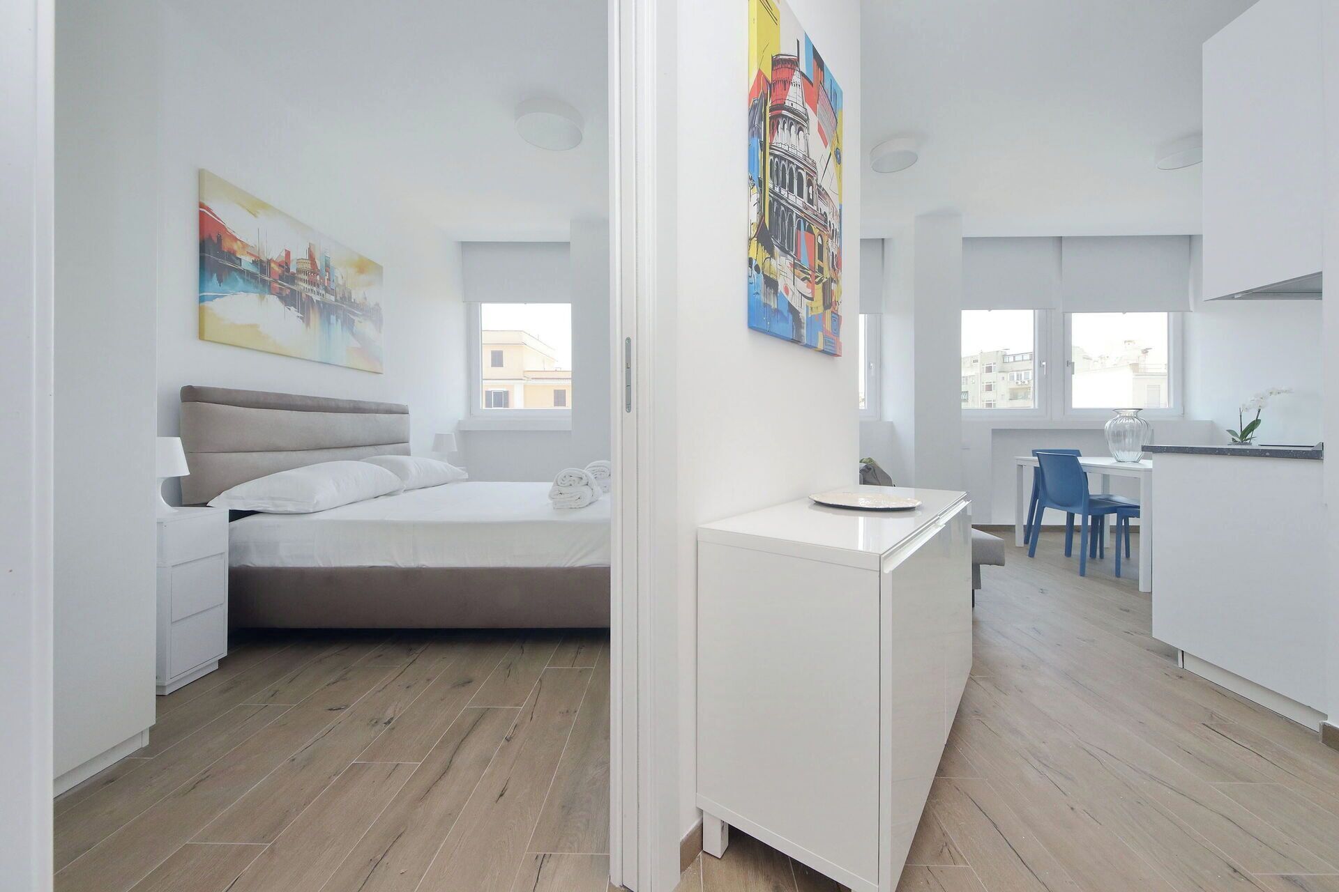 Een moderne, goed verlichte kamer met een bed, een bureau en een stoel. Er hangen schilderijen aan de muur en een raam zorgt voor natuurlijk licht.