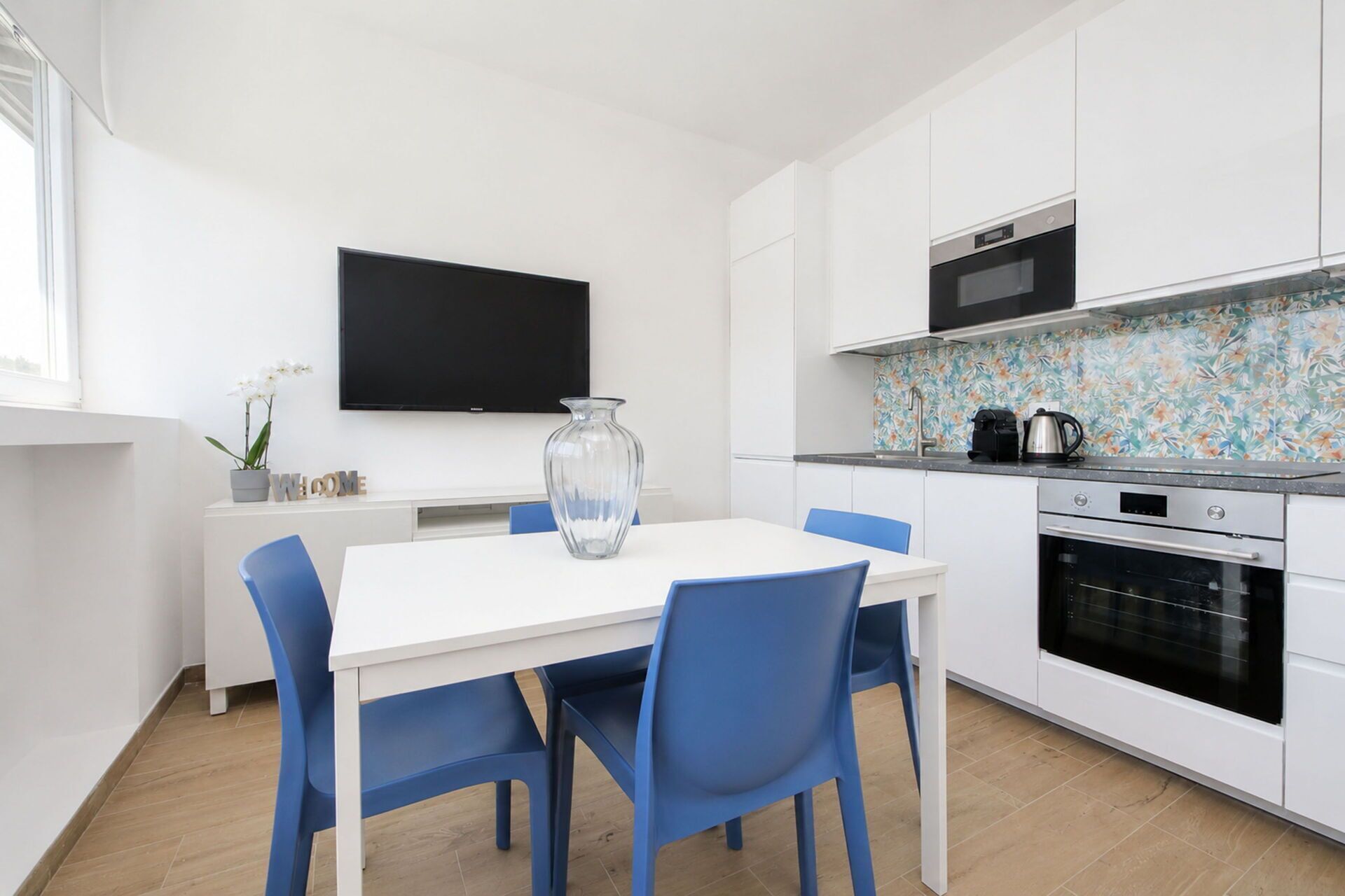 A modern kitchen with white cabinets, a flat-screen TV, a microwave, and a coffee maker.