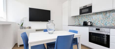 Una cocina moderna con armarios blancos, un televisor de pantalla plana, un microondas y una cafetera.