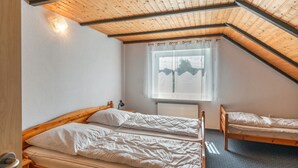 Una habitación con techo inclinado, dos camas, un ventanal con cortinas y un radiador.