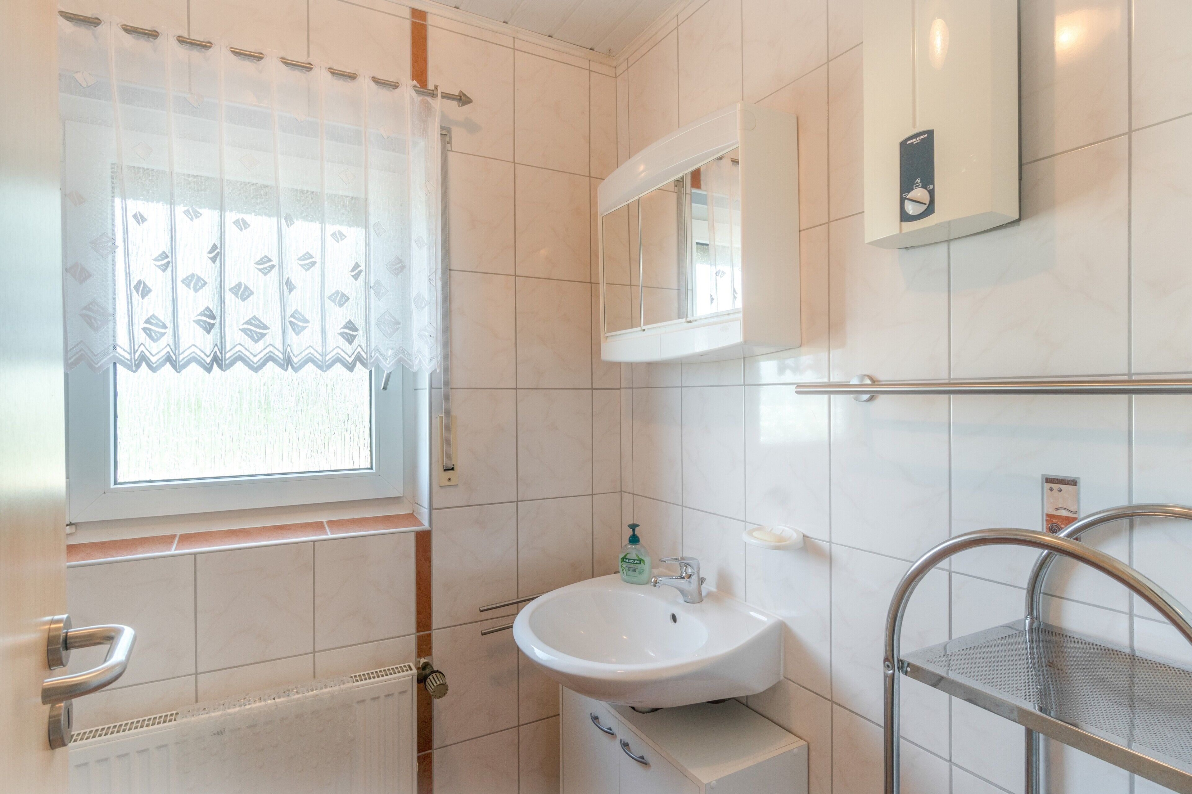 Ein Badezimmer mit Fenster, Waschbecken, Spiegel und Handtuchhalter.