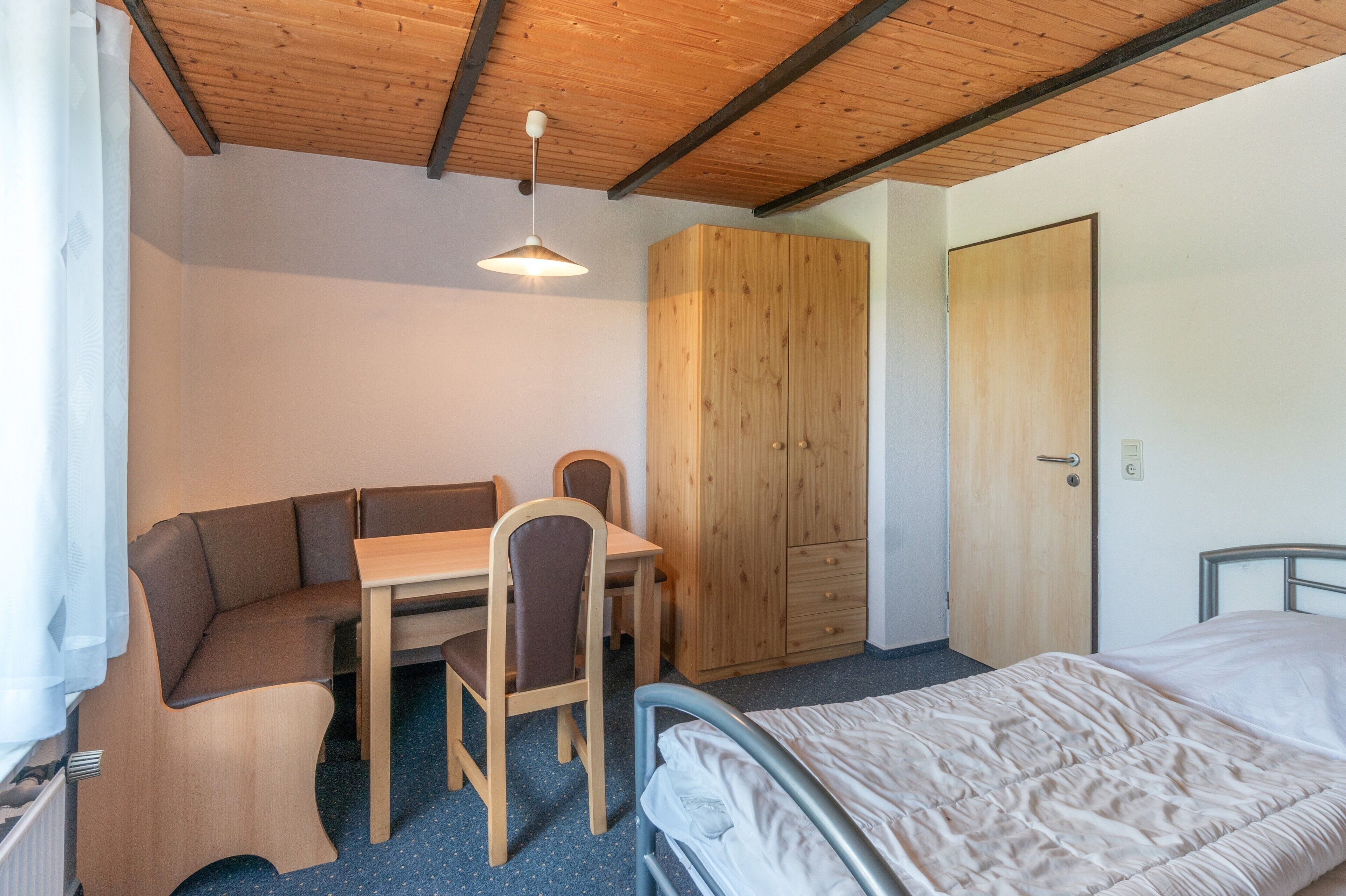 Ein Zimmer mit einem Bett, einem Schreibtisch mit Stuhl, einem Kleiderschrank und einer Hängelampe.