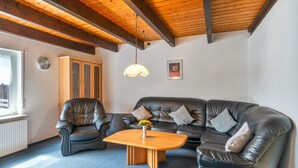 Una sala de estar con techo de madera, un sofá de cuero negro, un sillón de cuero, una mesa de centro de madera y un reloj de pared.