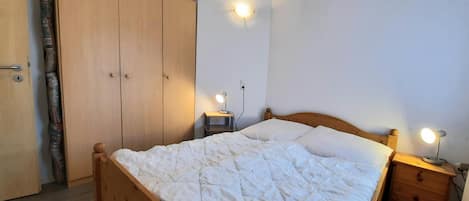 Une chambre à coucher avec un lit en bois, deux tables de chevet avec des lampes, une armoire et un luminaire fixé au mur.