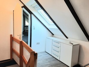 A room with a sloped ceiling, a wooden staircase, and a white cabinet with drawers. - Apartment 'FeWo 4 "Jan"' with Shared Garden (Dornum)