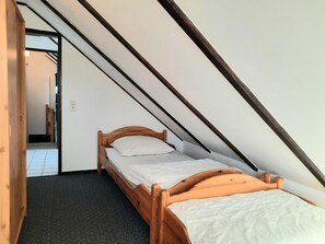 A single bed in a room with sloped ceilings, a visible door leading to another room, and a carpeted floor. - Apartment 'FeWo 4 "Jan"' with Shared Garden (Dornum)