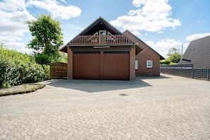 A two-story brick building with a garage, surrounded by a paved driveway and a metal fence. - Apartment 'FeWo 4 "Jan"' with Shared Garden (Dornum)