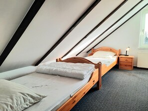 A small, single-bed room with a sloped ceiling, a wooden bed frame, a bedside table with a lamp, and a radiator. - Apartment 'FeWo 4 "Jan"' with Shared Garden (Dornum)
