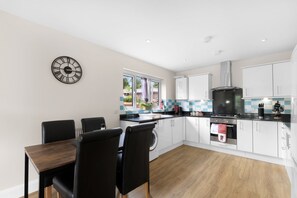 A modern kitchen with white cabinets, a black countertop, and a stainless steel range hood. - Heathrow Living 2BDR 2BA Apt by 360 Stays - Apt 09 (Stanwell)