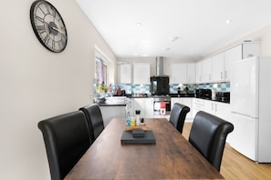 A modern kitchen with white cabinets, a black stove, and a wooden dining table with chairs. - Heathrow Living 2BDR 2BA Apt by 360 Stays - Apt 09 (Stanwell)