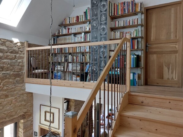 Un interno su più livelli con una scala in legno, scaffali e una parete in pietra.