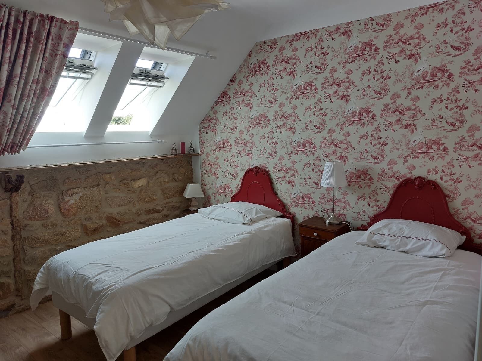 Una habitación con dos camas, una pared de piedra, una ventana con cortinas y un papel tapiz floral.