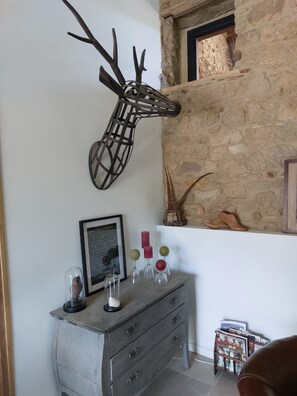 Ein rustikales Interieur mit einer Steinwand, einer Hirschdekoration, einem gerahmten Zitat, dekorativen Vasen und einer Kommode im Vintage-Stil.