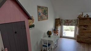 Et værelse med trægulv, et hvidt bord med en globus, en stol, en lyserød væg, et maleri og et vindue med udsigt.