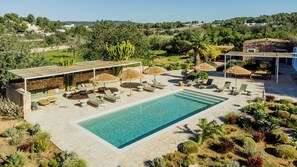 A pool area with lounge chairs and umbrellas, surrounded by landscaped gardens and a stone wall.