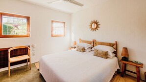 A bedroom with a bed, a chair, a bedside table, a lamp, and a ceiling fan.