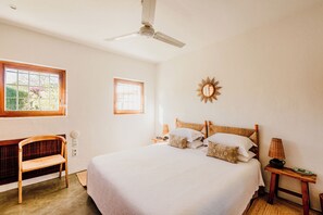 A bedroom with a bed, a chair, a bedside table, a lamp, and a ceiling fan.