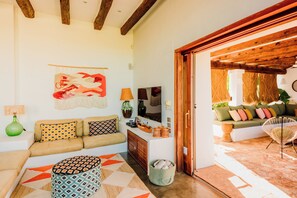Una sala de estar con un sofá, un tapete estampado, un jarrón verde y techo de madera.