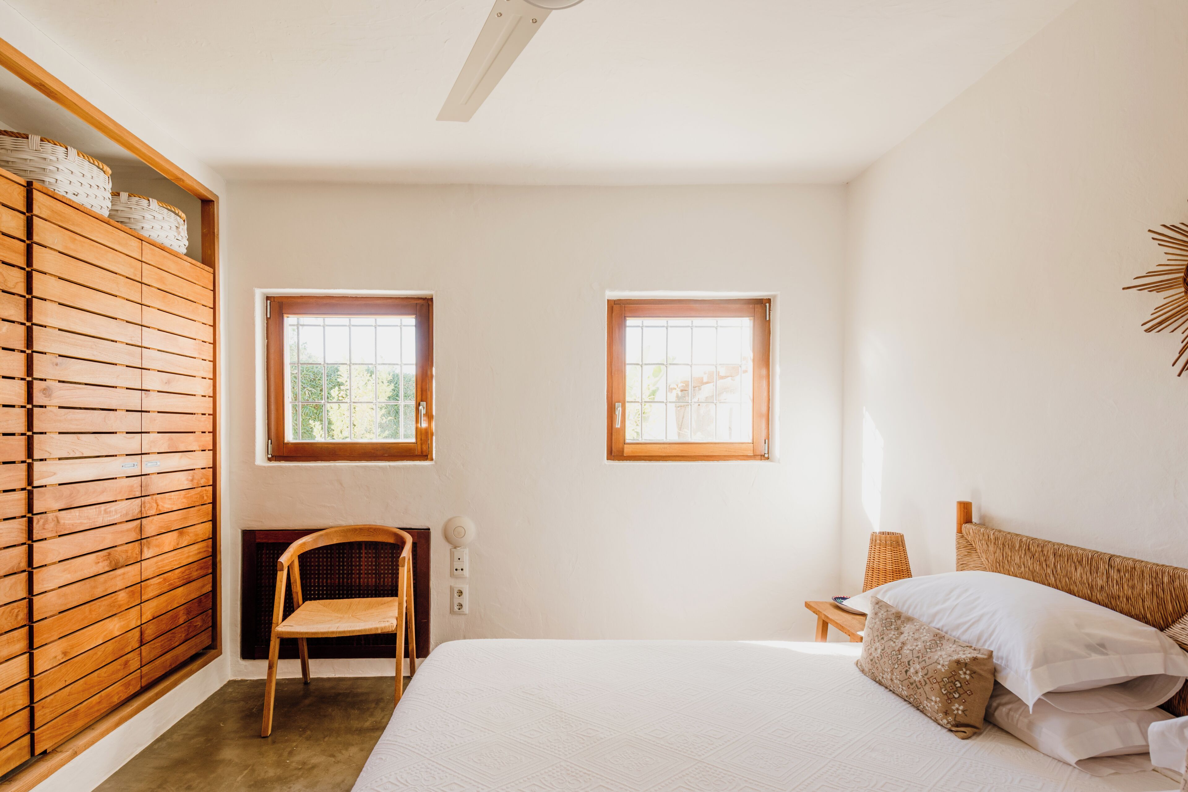 Ein Schlafzimmer mit einem Bett, zwei Fenstern, einem Sessel und einem kleinen Tisch.