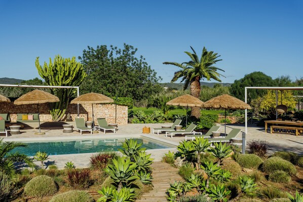 A poolside area with lounge chairs, thatched umbrellas, and a variety of plants.