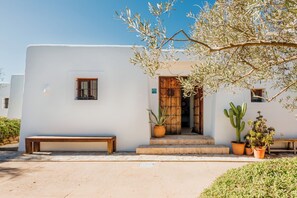 A white building with a wooden door, a bench, and potted plants.