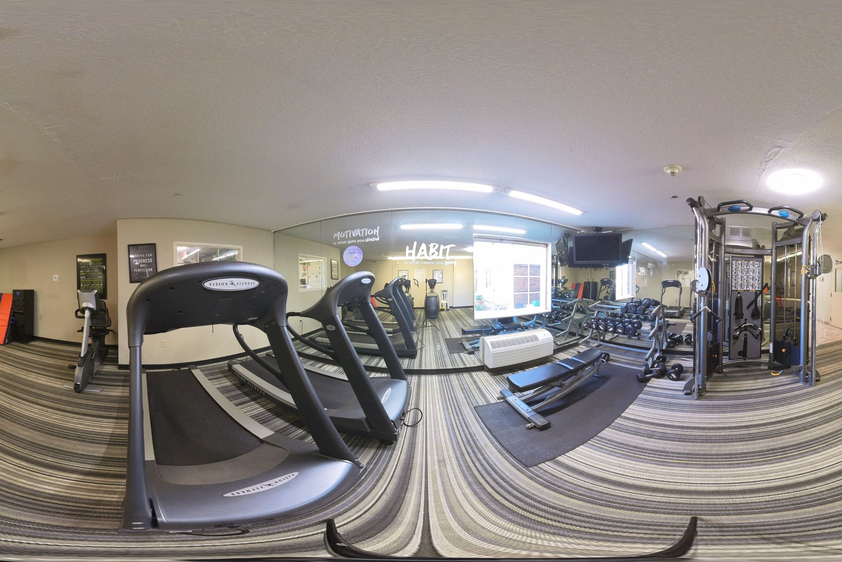 Ein Fitnessstudio mit Laufbändern, Gewichten und einer Spiegelwand.