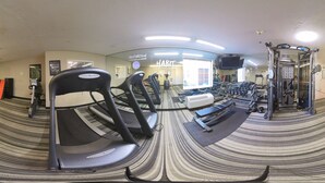 Une salle de sport équipée de tapis de course, de poids et d’un mur recouvert de miroirs.