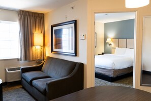 Habitación de hotel con sofá, cama, un cuadro en la pared, lámpara y ventana con cortinas.