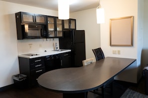 A modern kitchen with a built-in microwave, refrigerator, and a large dining table. - Coratel Suites Extended Stay MSP Airport Minneapolis-Queen Suite Kitchenette NS (Richfield)
