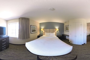 A hotel room with a curved bed, a television, a desk, and a wardrobe. - Coratel Suites Extended Stay MSP Airport Minneapolis-Queen Suite Kitchenette NS (Richfield)