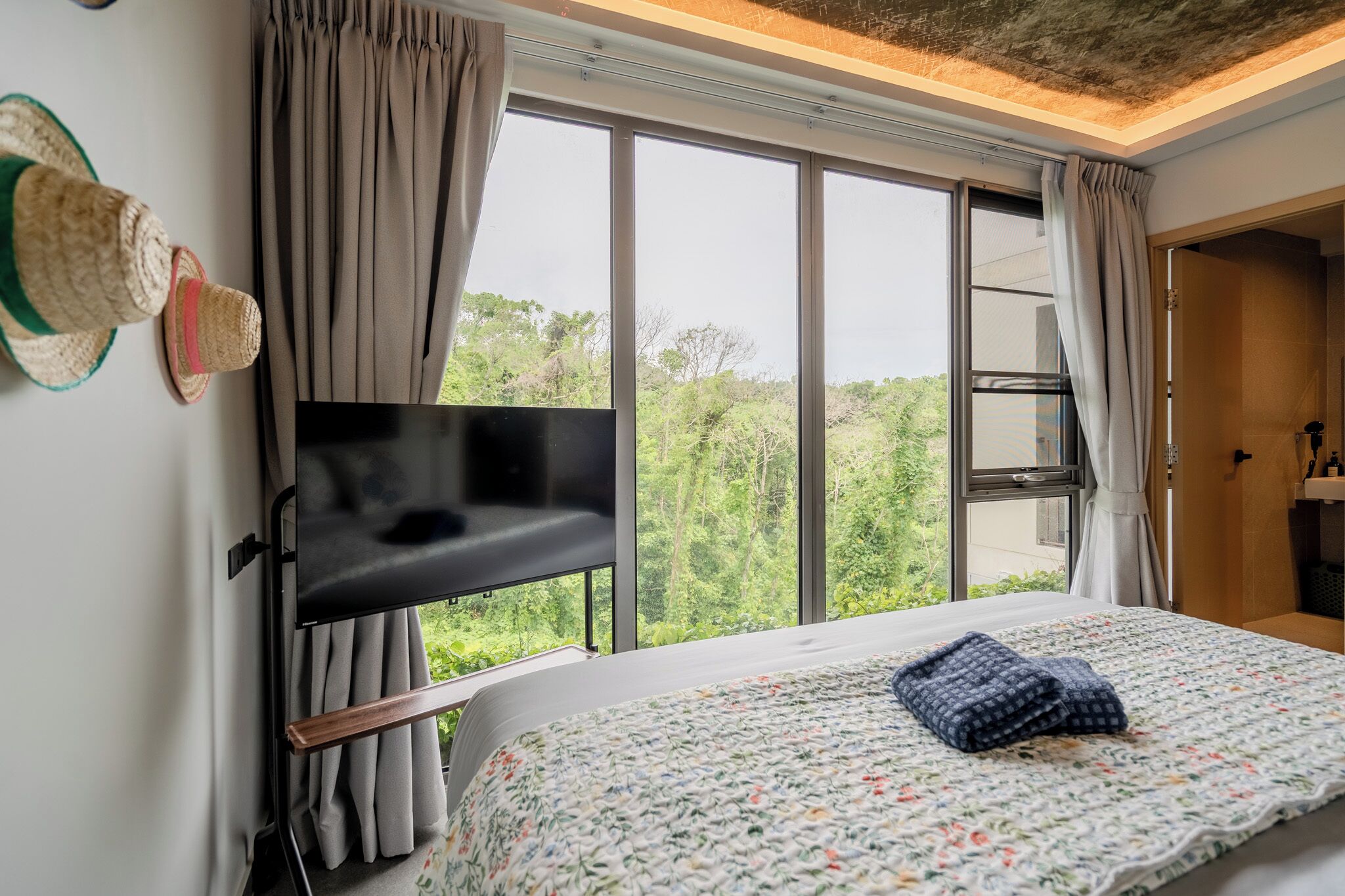 A bedroom with a bed, a television, and a window with curtains.