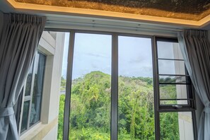 A room with large windows, a view of a forested hill, and a ladder leading to a window.