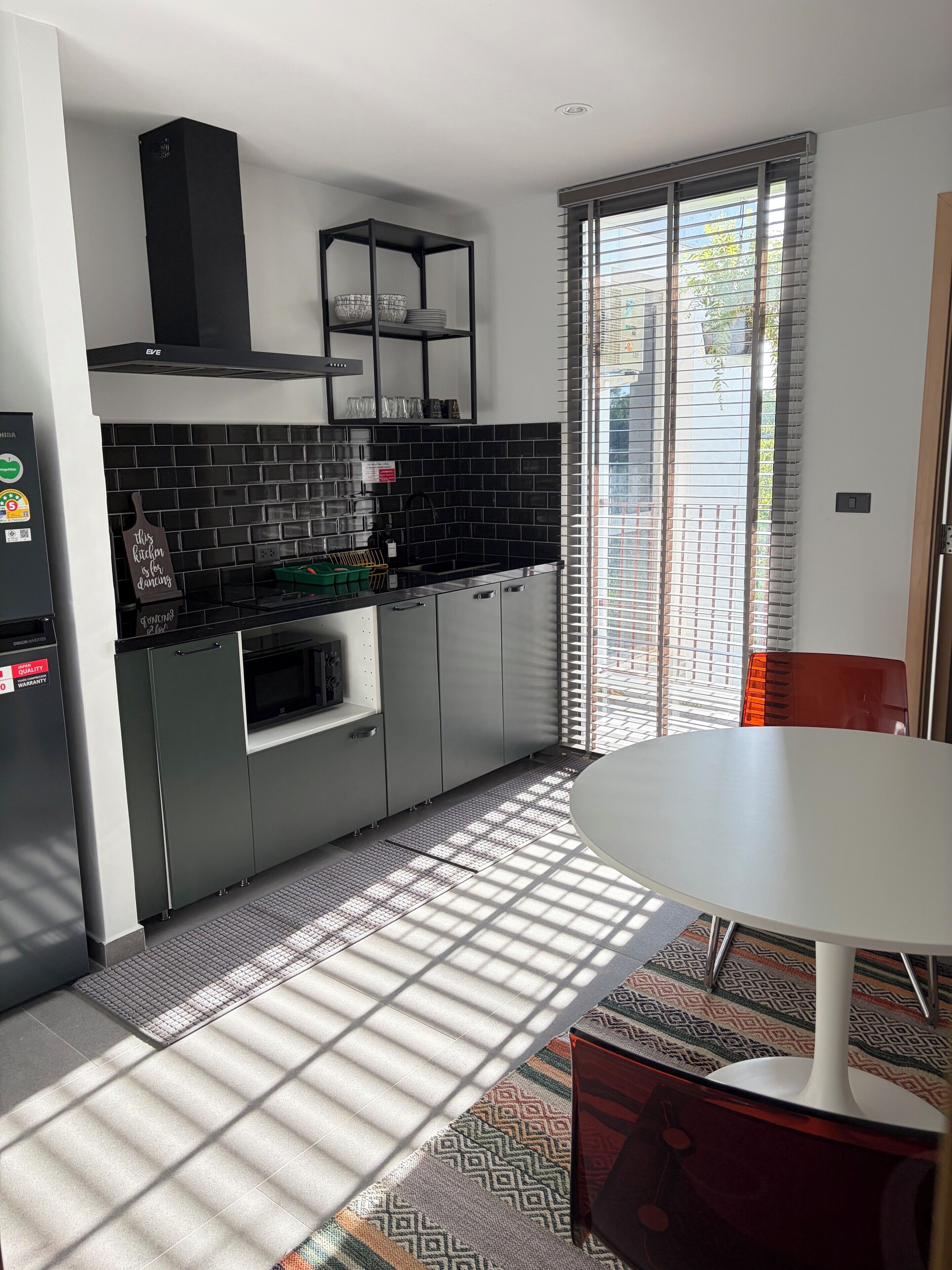Una cucina moderna con schienale nero, elettrodomestici in acciaio inossidabile e forno a incasso. C'è una zona pranzo con tavolo bianco e tappeto decorato.