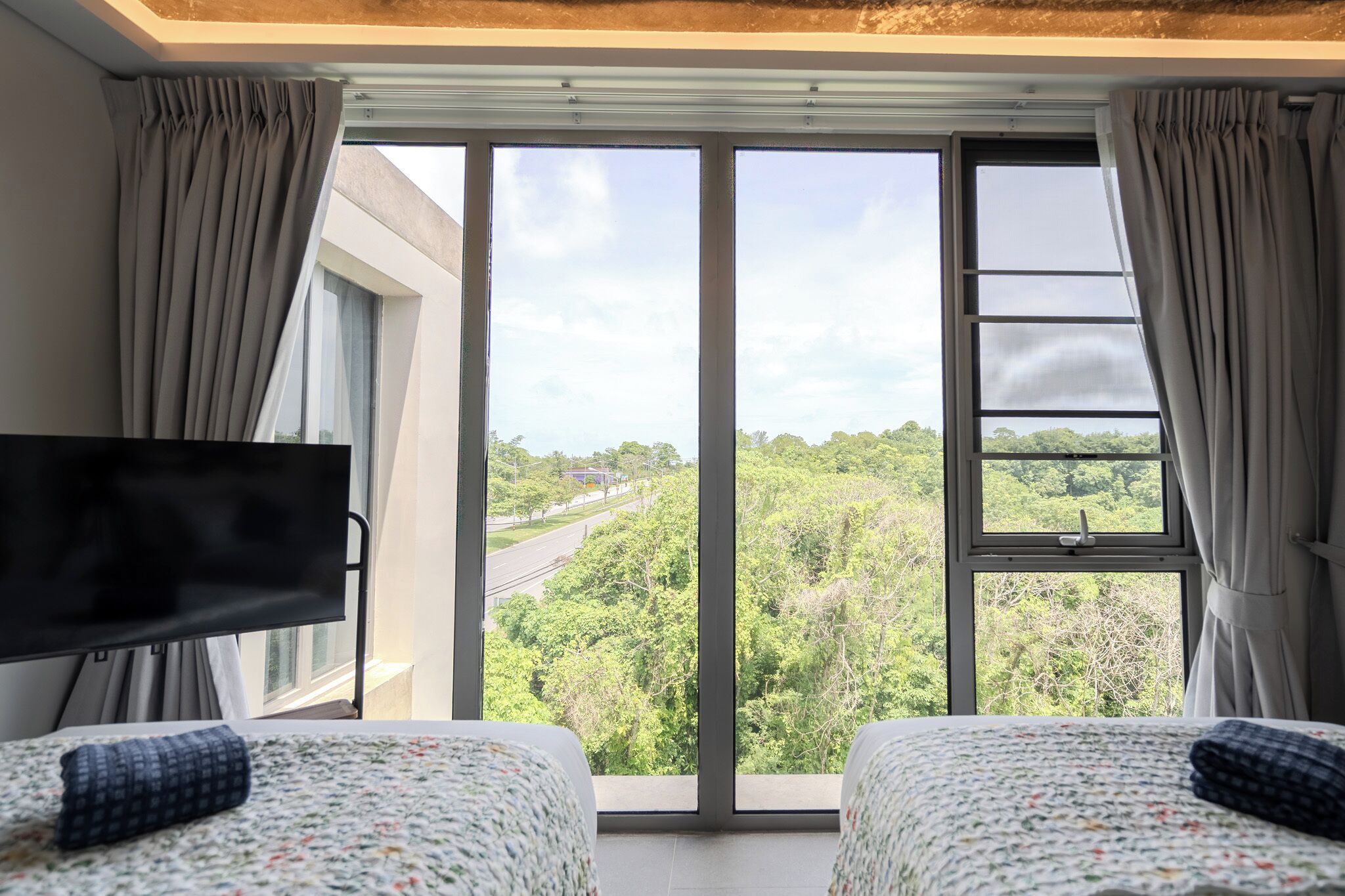 Habitación de hotel con dos camas, televisor y ventana grande que ofrece vistas a un paisaje verde.
