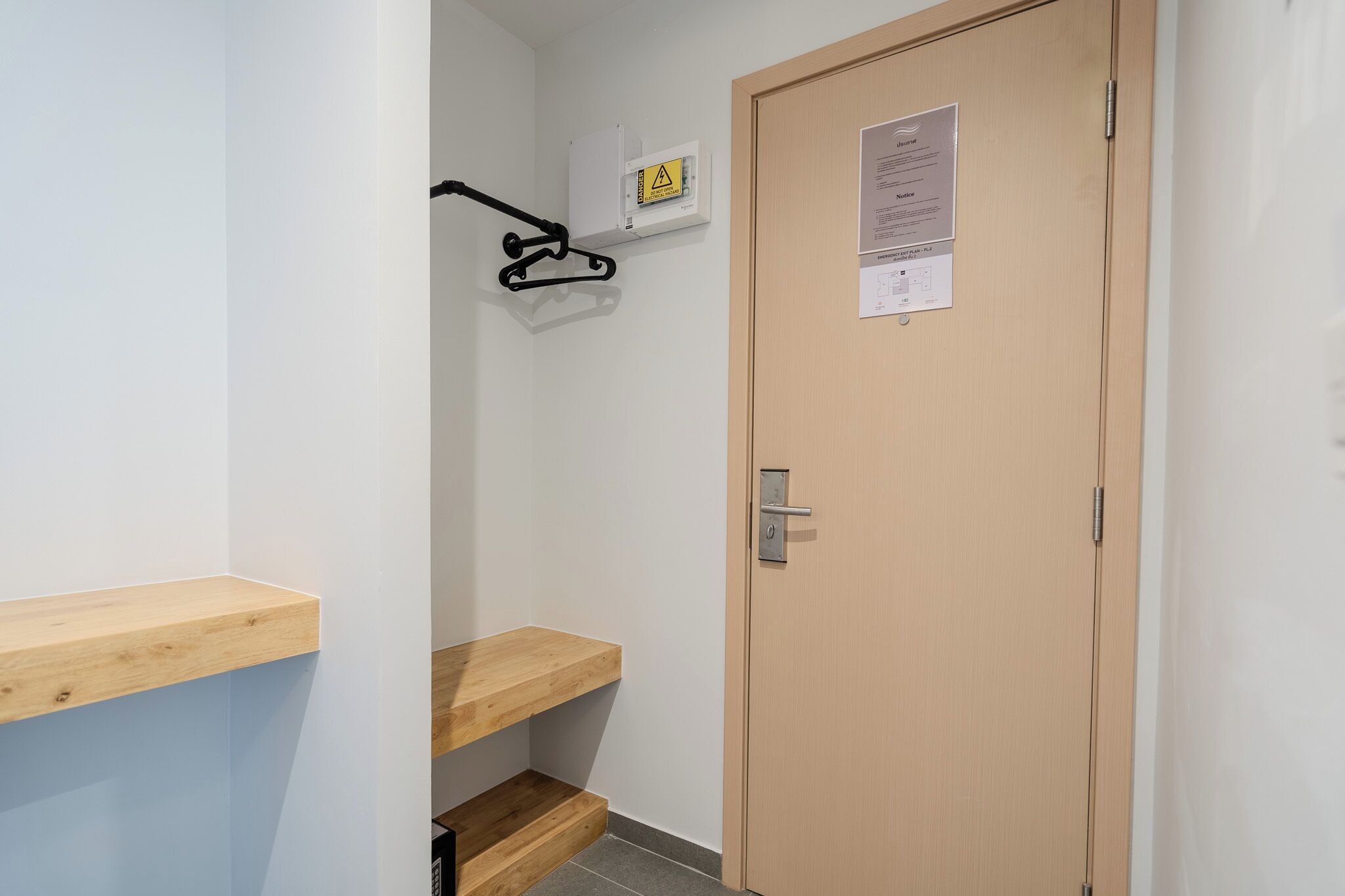 Un pasillo estrecho con una puerta de madera, un aviso en la puerta y una señal de advertencia de seguridad en la pared.
