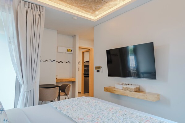 A hotel room with a bed, a television mounted on the wall, a small desk with a chair, and a bathroom visible through an open door.