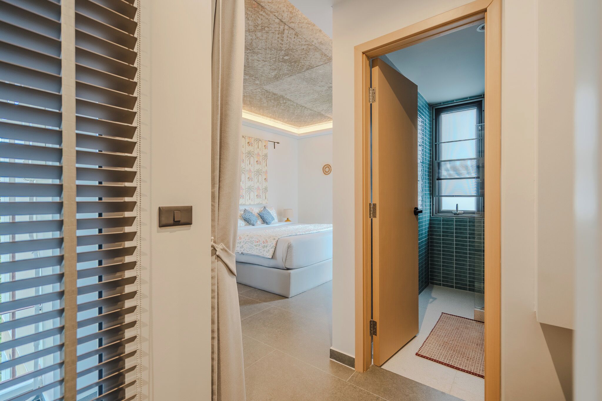 A hotel room with a bed, a bathroom with a tiled wall, and a door leading to another room.