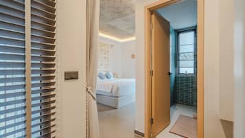 A hotel room with a bed, a bathroom with a tiled wall, and a door leading to another room.